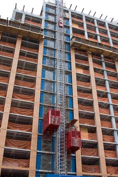 Two red elevators on the side of a tall building under construction