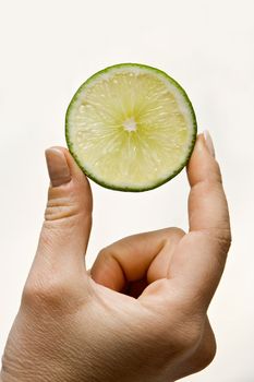 Woman hand holding up a wedge of lime, isolated on white