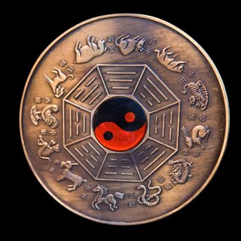 Lunar calendar depicted in a bronze medallion with a red and black ying yang in the middle, isolated on black