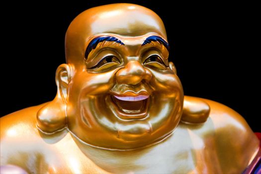 The gold colored face of a statue of a smiling Buddha, isolated on black