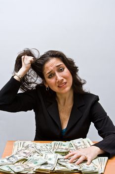 Business woman pulling hair and stressed about finances. Sitting at a table with lots of money. Isolated on a white background
