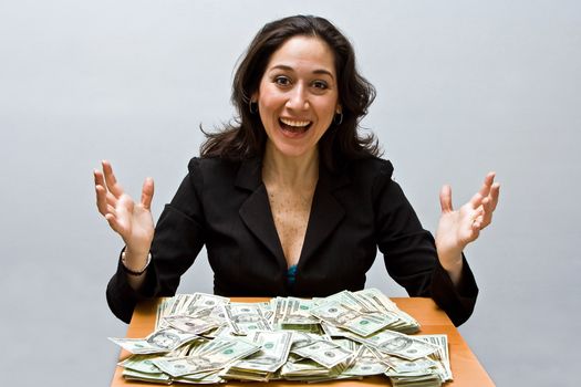 Happy business woman sitting at a table covered with stacks of money isolated on a white background