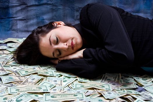 Rich business woman laying with her money as she dreams about it isolated on a dark background