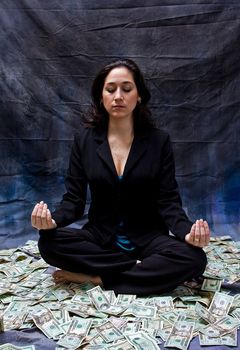 Rich woman meditating while sitting in money isolated on a dark background