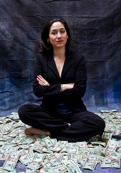 Rich woman sitting with crossed arms in money isolated on a dark background