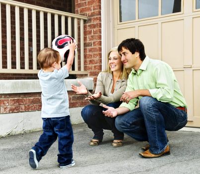 Happy young family playing soccer with toddler on driveway