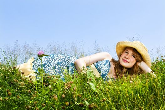 Young teenage girl laying on summer meadow in straw hat