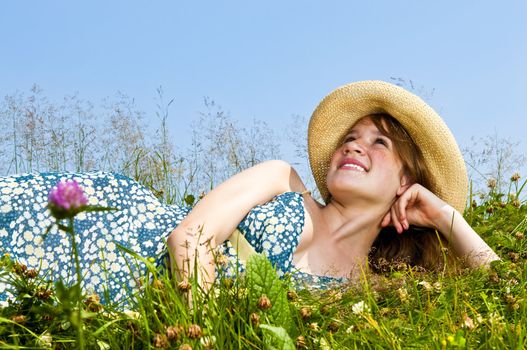 Young teenage girl laying on summer meadow in straw hat looking up