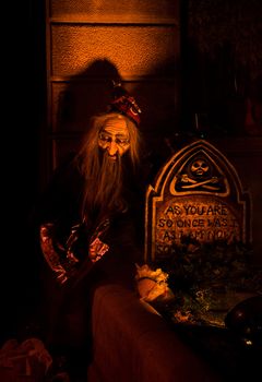 Old bearded man (puppet) sitting at a graveyard at a lit up tomb; a Halloween set-up