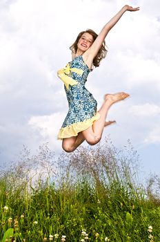 Young teenage girl jumping in summer meadow amid wildflowers