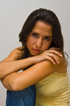 a beautiful dark brown haired latina woman wearing a yellow shirt and arms crossed on top of her knee, isolated on white