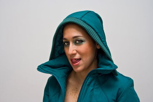 A sexy young woman licking her lips, wearing a green winter coat zipped open and the hood covering her head, isolated on white