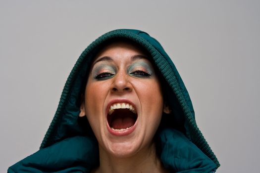 A beautiful young woman screaming aggressively wearing a green winter coat and the hood over her head, isolated on white