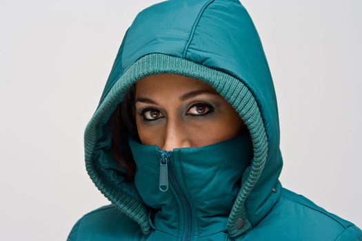 A young woman wearing a green winter coat using the hood to cover her head so that only her eyes are visible, isolated on white