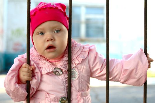 Curious pretty little girl behind old railing (grille).