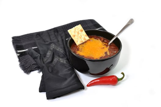Bowl of chili with melted cheese, red cayenne pepper,cracker, spoon, gloves, and scarf.  Isolated on white background.