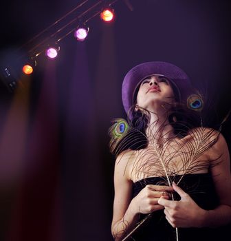 Portrait of young trendy girl holding peacock feathers under disco lights background