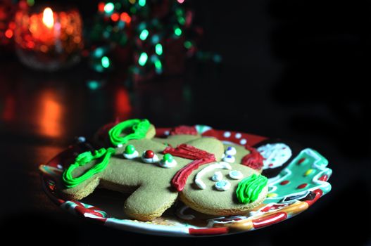 Gingerbread men on plate with candle isolated on black background.