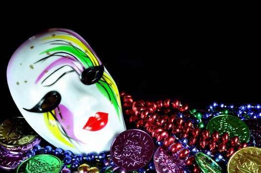 Mardi Gras mask with beads and doubloons on black background with copy space. 