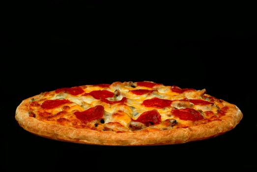 Whole pepperoni pizza with tomatoes in background.  Isolated on black background. 
