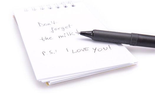 Closeup of a notebook with a shopping reminder on it and a black pen. Isolated on white.
