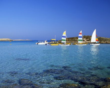 Bright pleasure sailboats by rocks in the shallow water of Nissi Beach, Cyprus