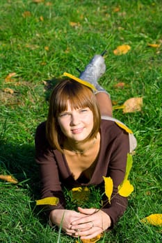The young girl on a green grass in autumn park during a leaf fall