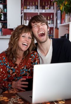 Laughing couple using a computer at a coffee house
