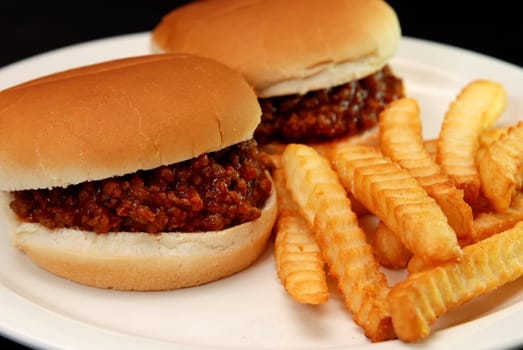 Two sloppy joe burgers and crinkle cut french fries isolated on black background.