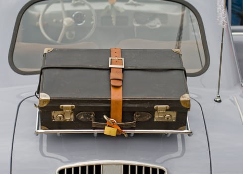 An old suitcase on the back of an old car