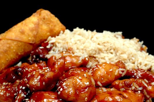 Chinese food.  Sesame chicken with egg roll on black background.