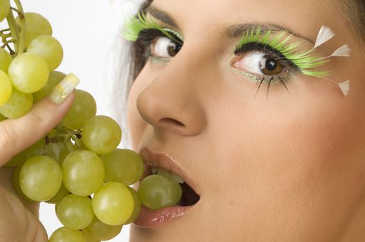 close up of a sensual girl with green eyelashes and grape between lips