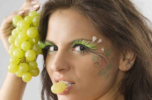 nice girl with a grape between the lips and her face painted with leaf