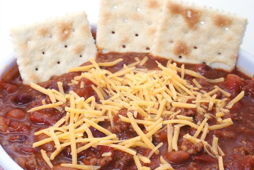 Closeup of hot bowl of chili with beans, cheese, and crackers. 