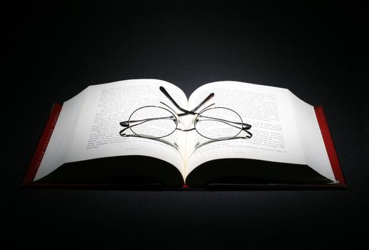 open book with a pair of eye glasses on dark background
