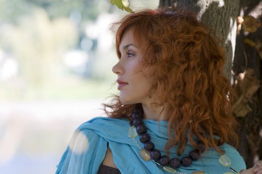 cute red haired girl in autumn dress near a tree looking one side focus on hair