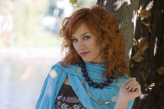 close up of a cute red haired girl with sky-blue scarf necklace near a tree