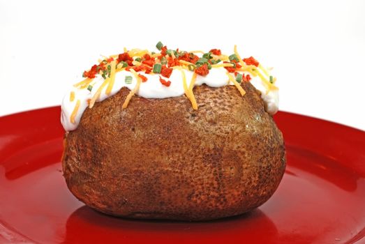 Baked potato loaded with butter, sour cream, cheddar cheese, bacon bits, and chives.  Isolated on white background.