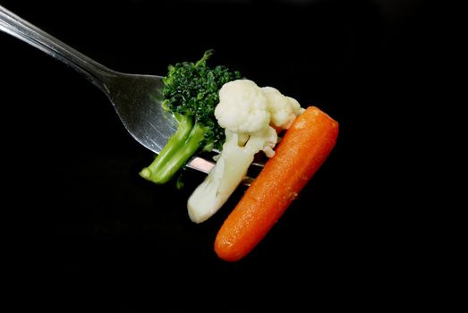 Broccoli, cauliflower, and carrot on fork isolated on black background.