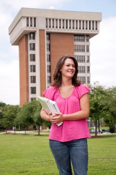 Female college student standing in front of school with books in hand. 