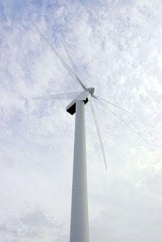 a wind turbine against a calm cloudy sky with movement of the blades