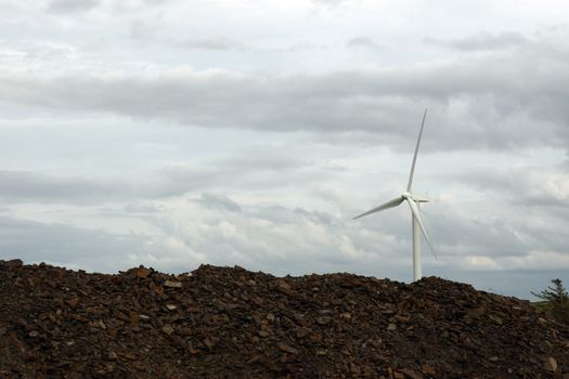 a wind turbine against a calm cloudy sky with rock piles in foreground