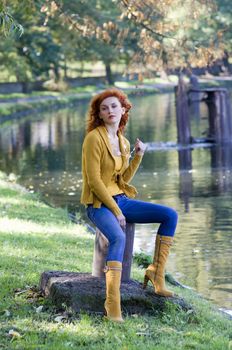 beautiful woman sitting near river in yellow casual autumn dress