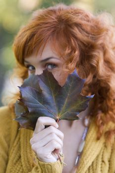 close up of red-haired woman behind a leaf in park focus on leaf