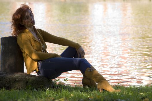 cute young woman laying on the grass near the river in autumn color