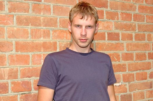 Young stylish man with blonde hair stand near brick wall.