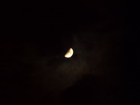 Half moon in a black night sky with light clouds.