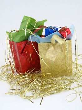 Two foiled gift bags full of wrapped presents. On a bed of gold tinsel over a white background.