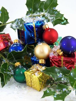 Colorful gift boxes, Christmas bulbs and holly, sprinkled with artificial snow. Isolated on a white background.