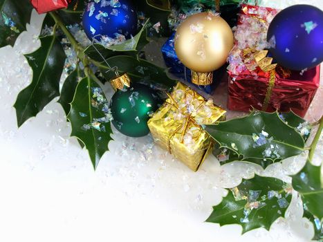 Colorful gift boxes, Christmas bulbs and holly, sprinkled with artificial snow. Isolated on a white background.